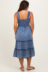 woman wearing a blue denim maternity dress with a smocked bodice and tiered skirt, showing her back