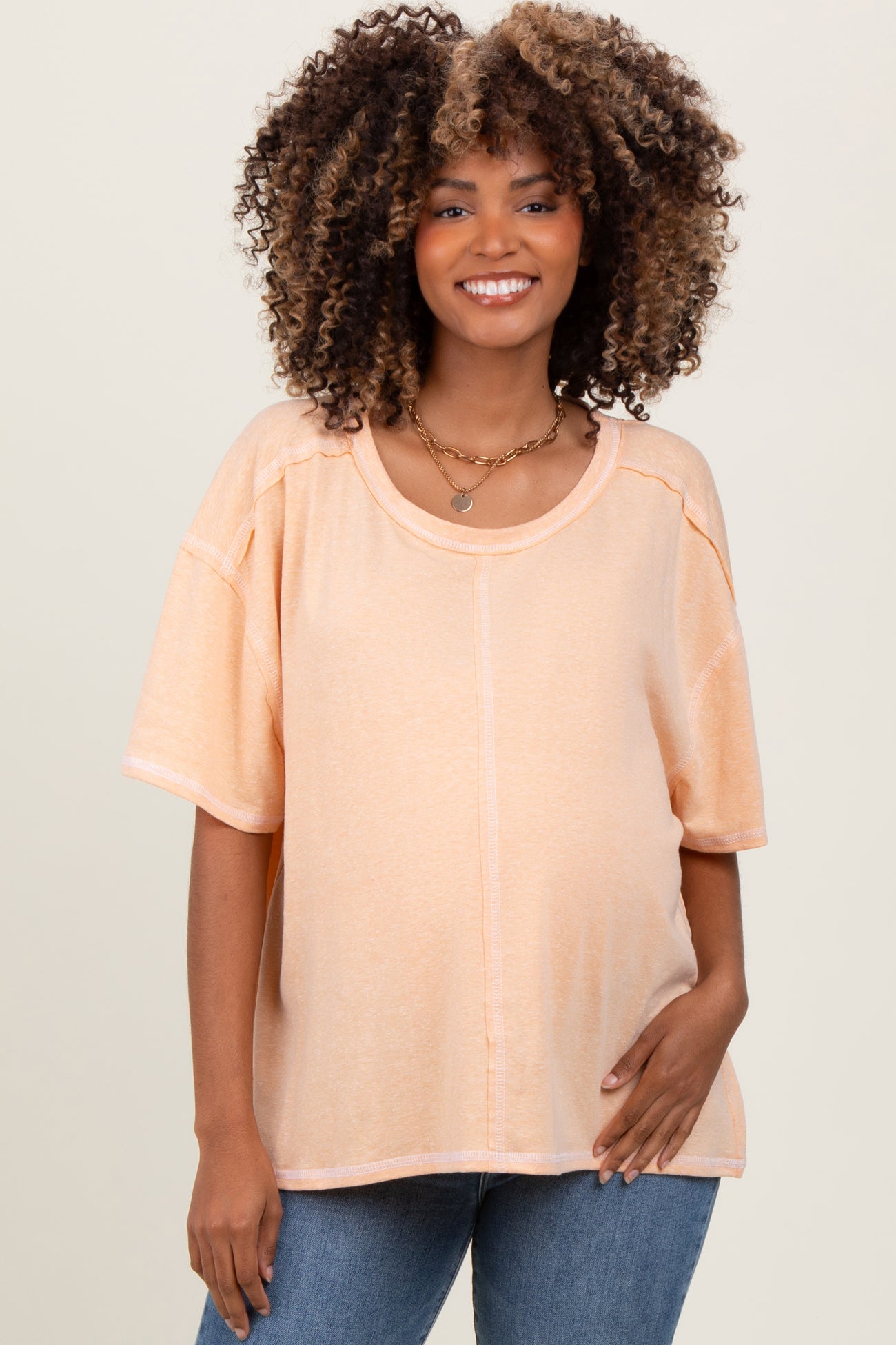 woman wearing a light peach maternity top with short sleeves and a relaxed fit, showing her baby bump