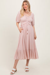 woman wearing a light pink midi dress with puff sleeves, a smocked bodice, and a tiered hem, standing and smiling