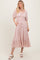 woman wearing a light pink midi dress with puff sleeves, a smocked bodice, and a tiered hem, standing and smiling