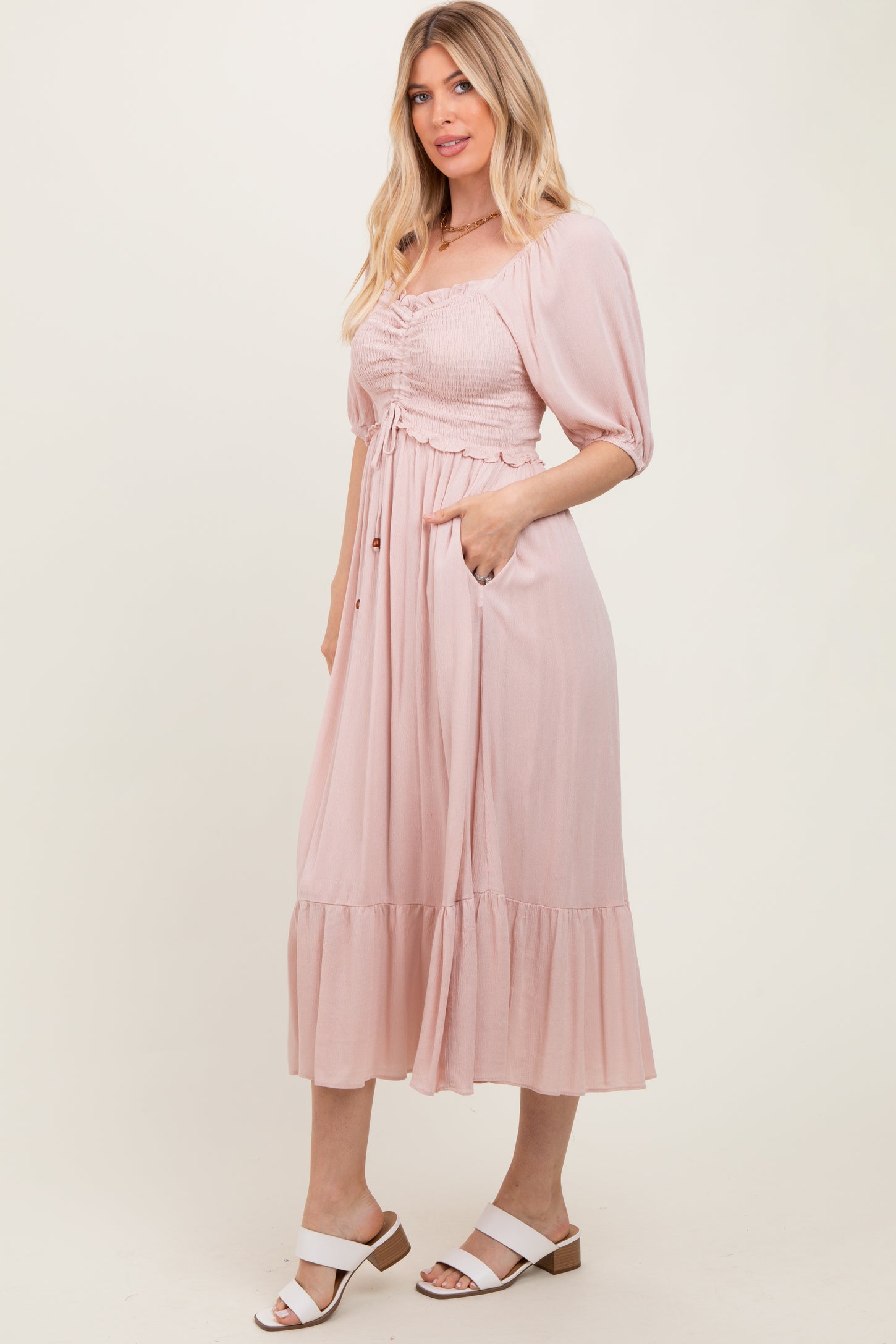 woman wearing a blush pink midi dress with puff sleeves and a ruched bodice, featuring a tiered skirt and pockets