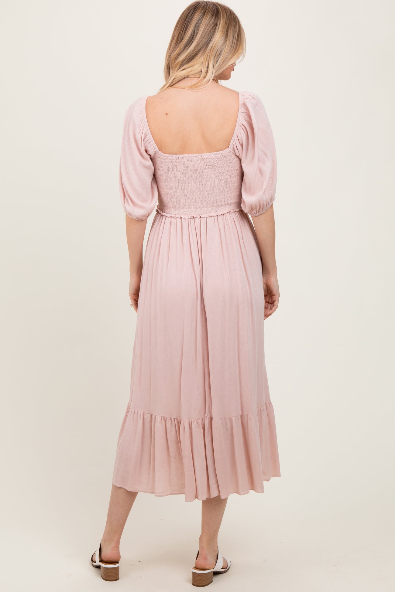 woman wearing a light pink smocked back midi dress with puff sleeves and a tiered skirt