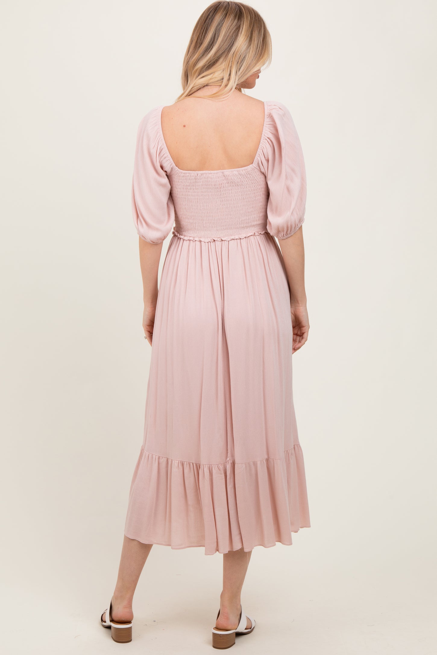 woman wearing a light pink smocked back midi dress with puff sleeves and a tiered skirt