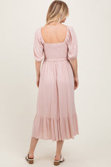 woman wearing a light pink smocked back midi dress with puff sleeves and a tiered skirt