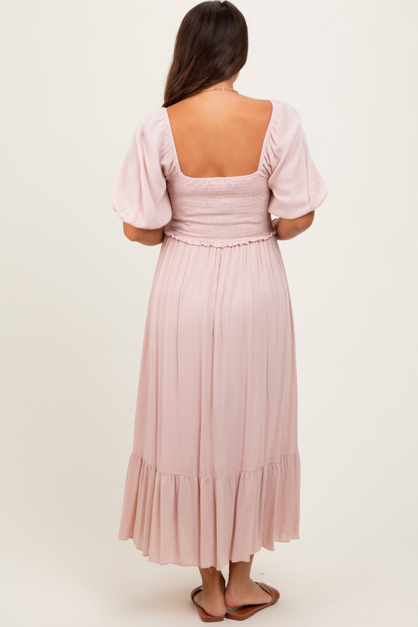 woman wearing a blush pink short sleeve smocked back maternity dress with a flowing skirt