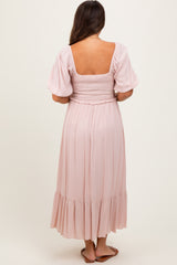 woman wearing a blush pink short sleeve smocked back maternity dress with a flowing skirt
