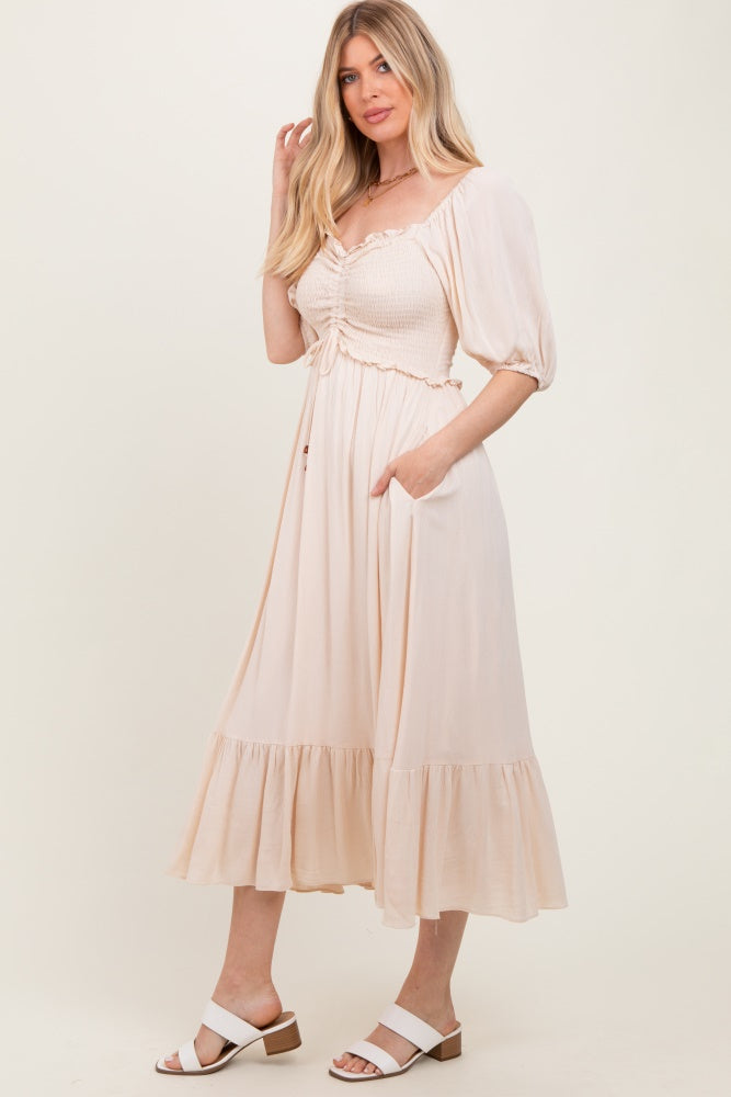 woman wearing a light pink midi dress with smocked bodice and puff sleeves, featuring a ruffled hem and side pockets