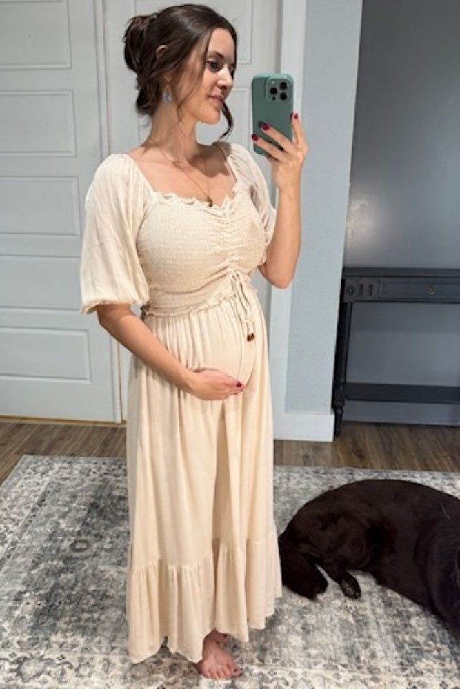 woman wearing a beige maternity maxi dress with smocked bodice and short puff sleeves, showing her baby bump