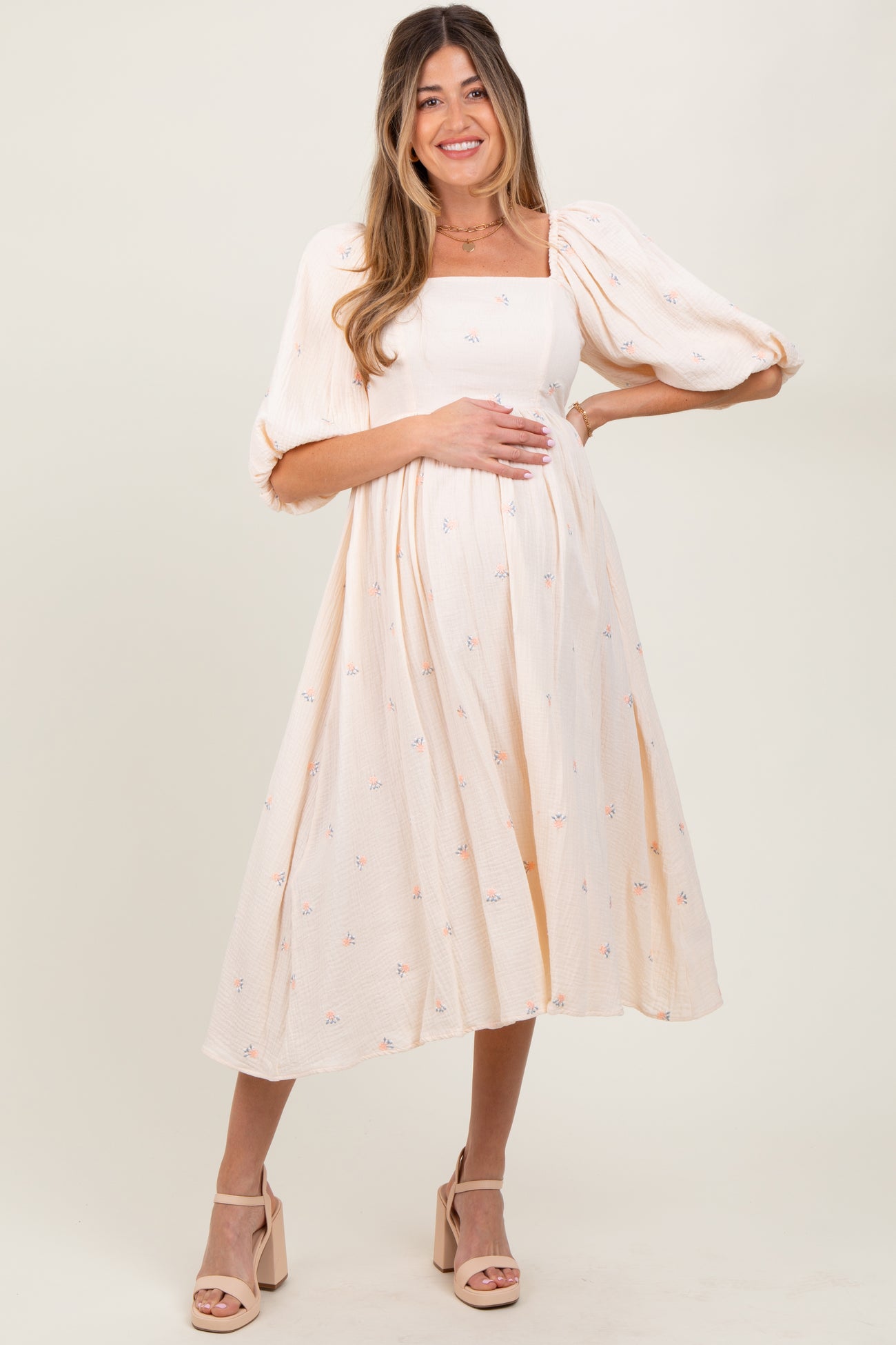 woman wearing a cream puff sleeve maternity dress with floral embroidery and a baby bump