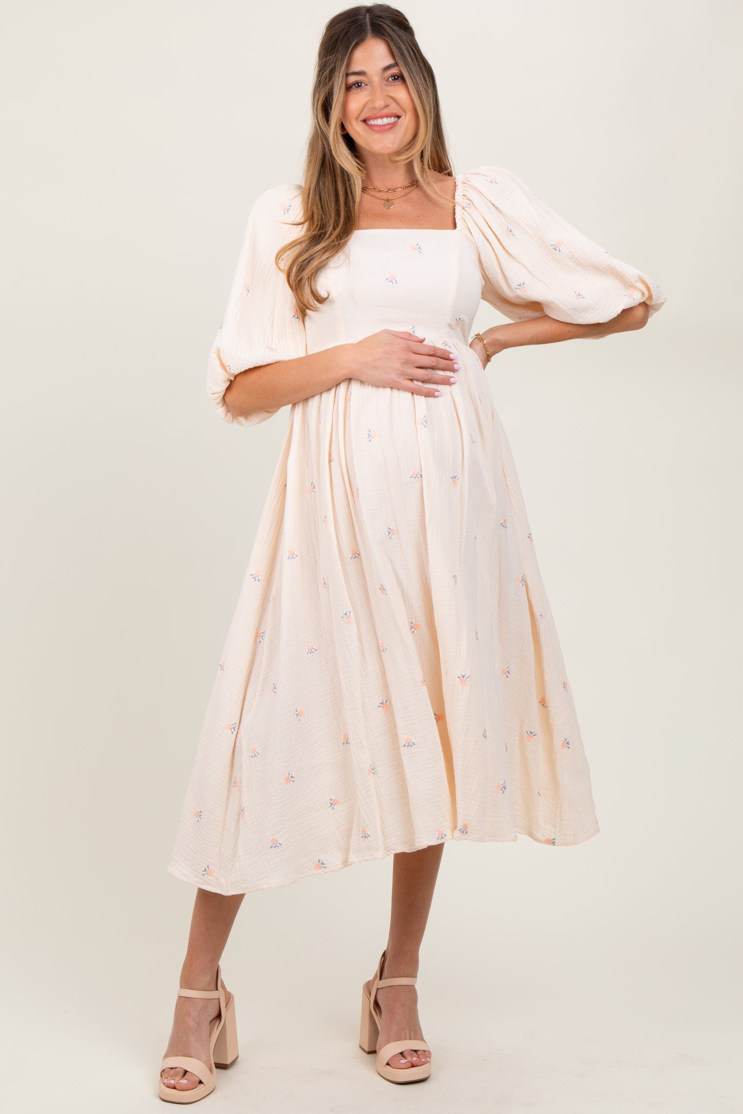 woman wearing a cream puff sleeve maternity dress with floral embroidery and a baby bump
