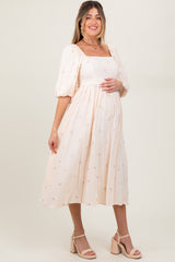 woman wearing a light pink maternity dress with puff sleeves and floral embroidery, holding her baby bump