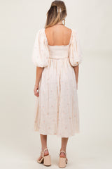 woman wearing a light pink maternity dress with puff sleeves and floral details, showing a gathered waist and back view