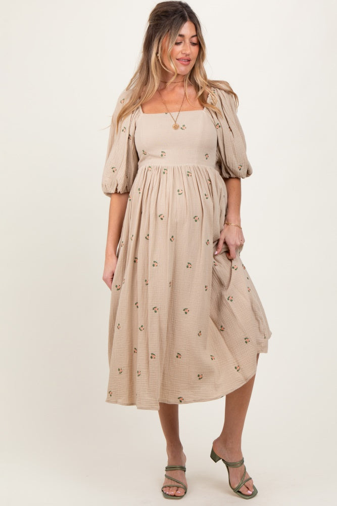 woman wearing a beige maternity dress with floral designs and puff sleeves, standing with a relaxed pose