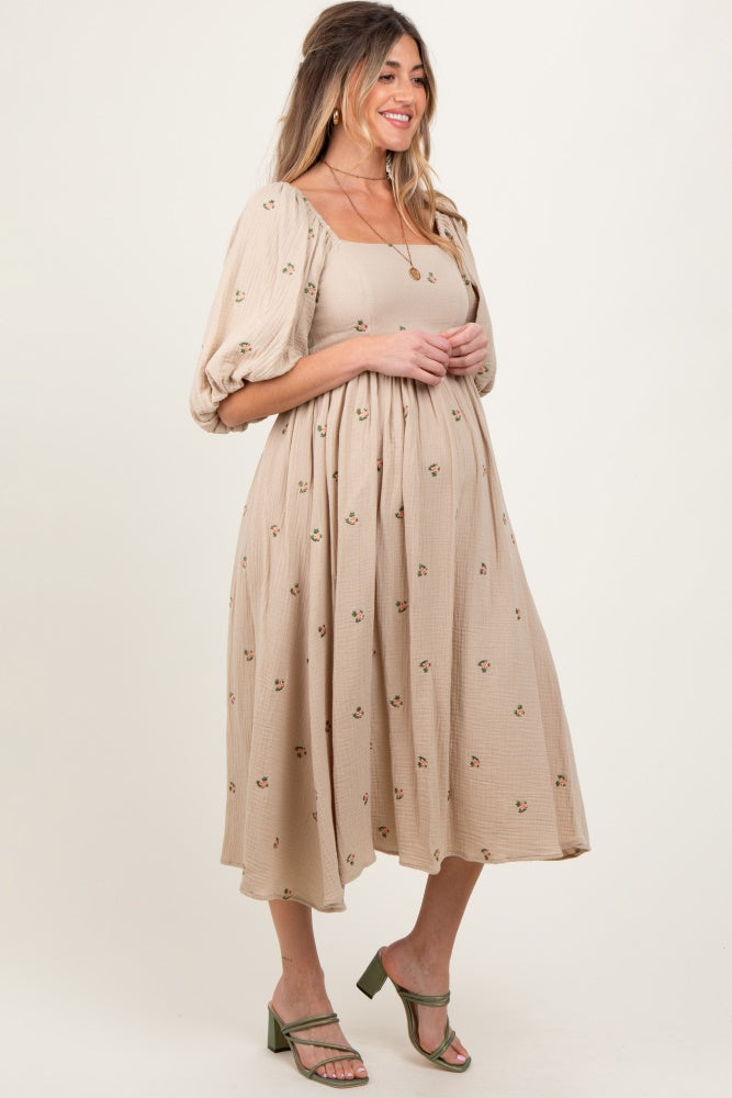 woman wearing a beige maternity dress with floral embroidery and puff sleeves, showing her baby bump