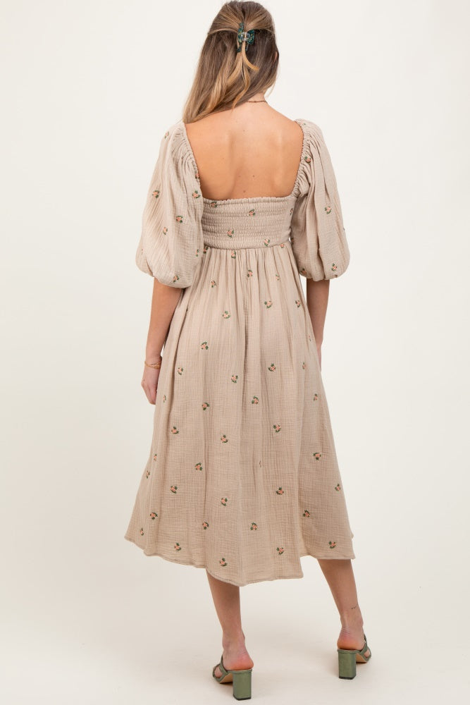 woman wearing a beige maternity dress with puff sleeves and floral embroidery, showing a baby bump from the back