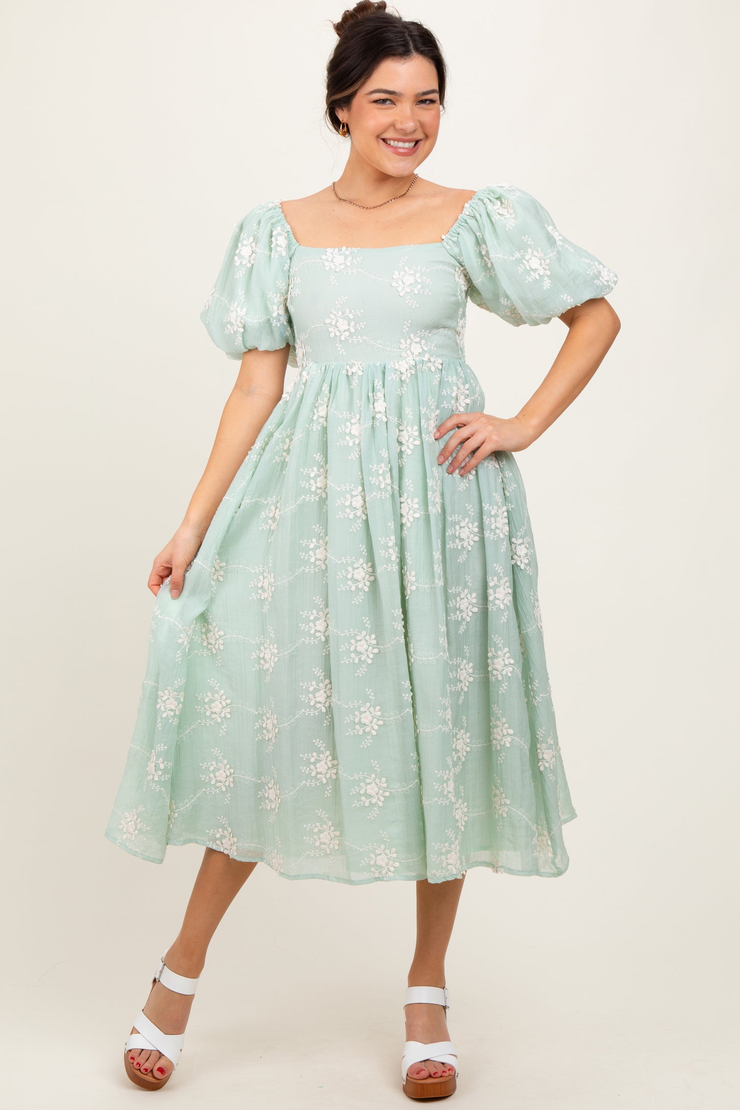 woman wearing a light green floral midi dress with puff sleeves and a square neckline, posing in a studio setting