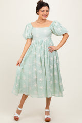woman wearing a light green floral midi dress with puff sleeves and a square neckline, posing in a studio setting