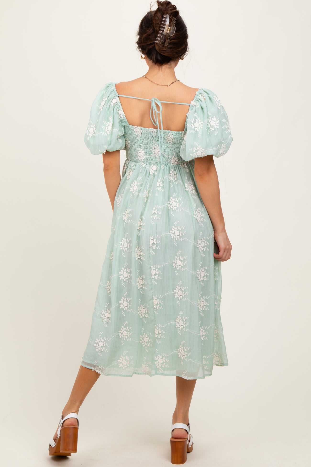 woman wearing a mint green puff sleeve dress with floral embroidery and a tied back detail