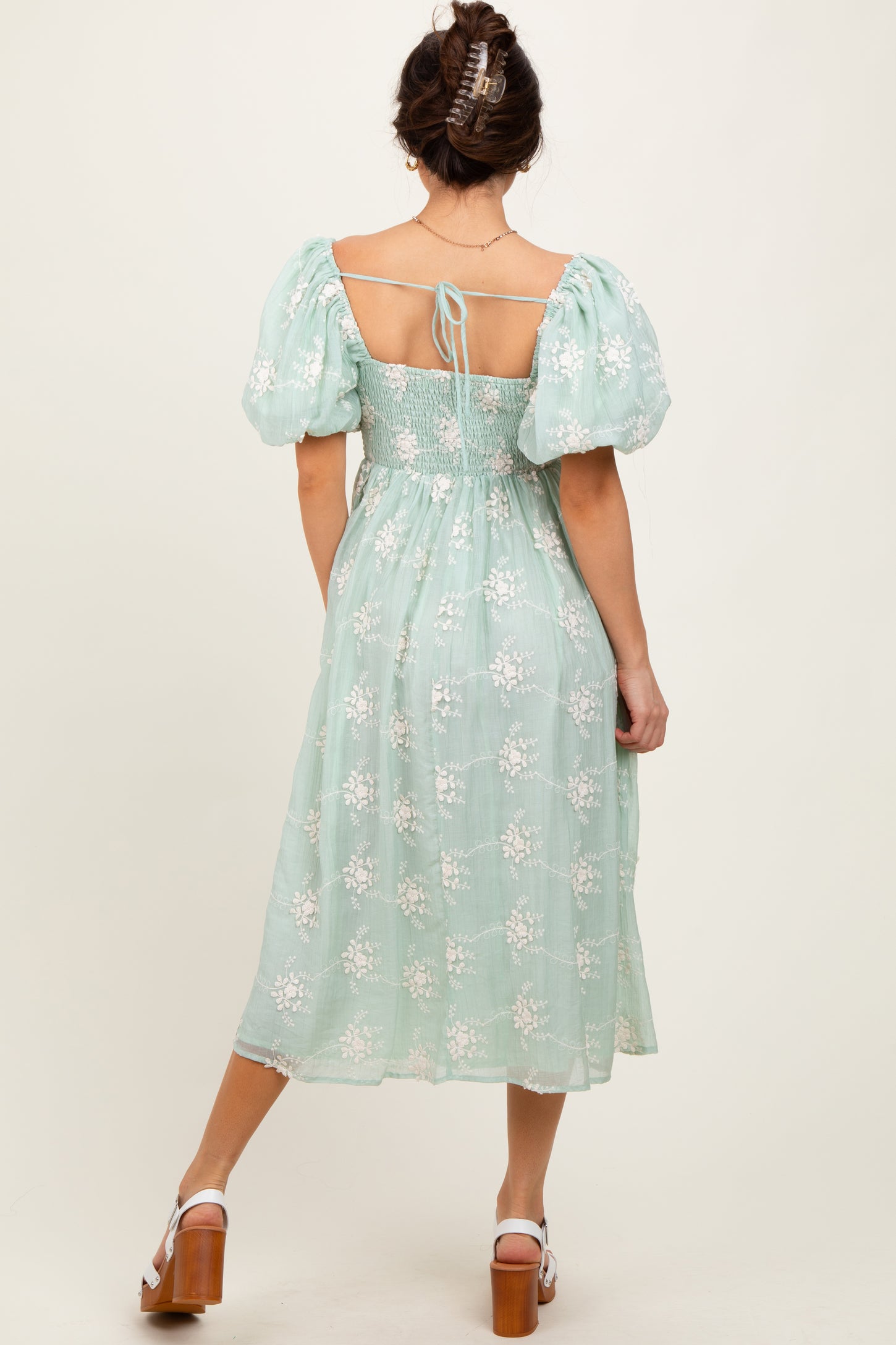 woman wearing a mint green puff sleeve dress with floral embroidery and a tied back detail