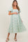 woman wearing a mint green floral maternity dress with puff sleeves and a cinched waist, holding her baby bump