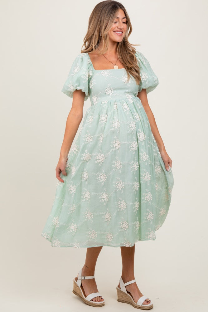 woman wearing a mint green maternity dress with puff sleeves and floral embroidery, showing her baby bump