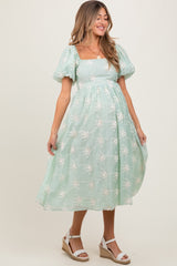 woman wearing a mint green maternity dress with puff sleeves and floral embroidery, showing her baby bump
