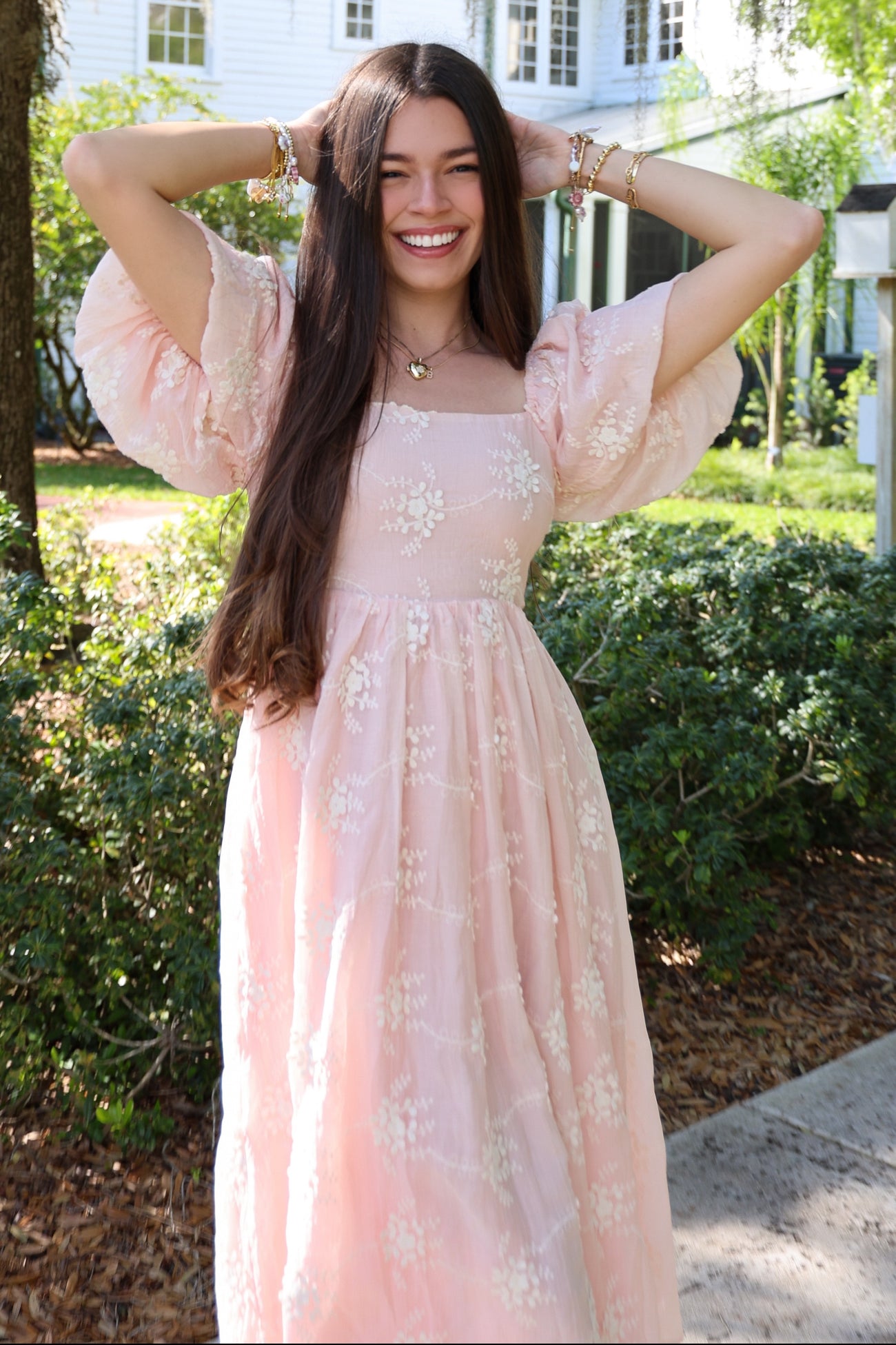 woman wearing a light pink floral maxi dress with puff sleeves and a square neckline, smiling outdoors