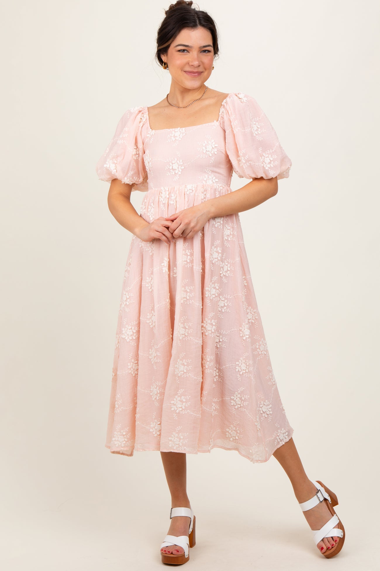 woman wearing a pink midi dress with puff sleeves and floral embroidery, standing against a neutral background
