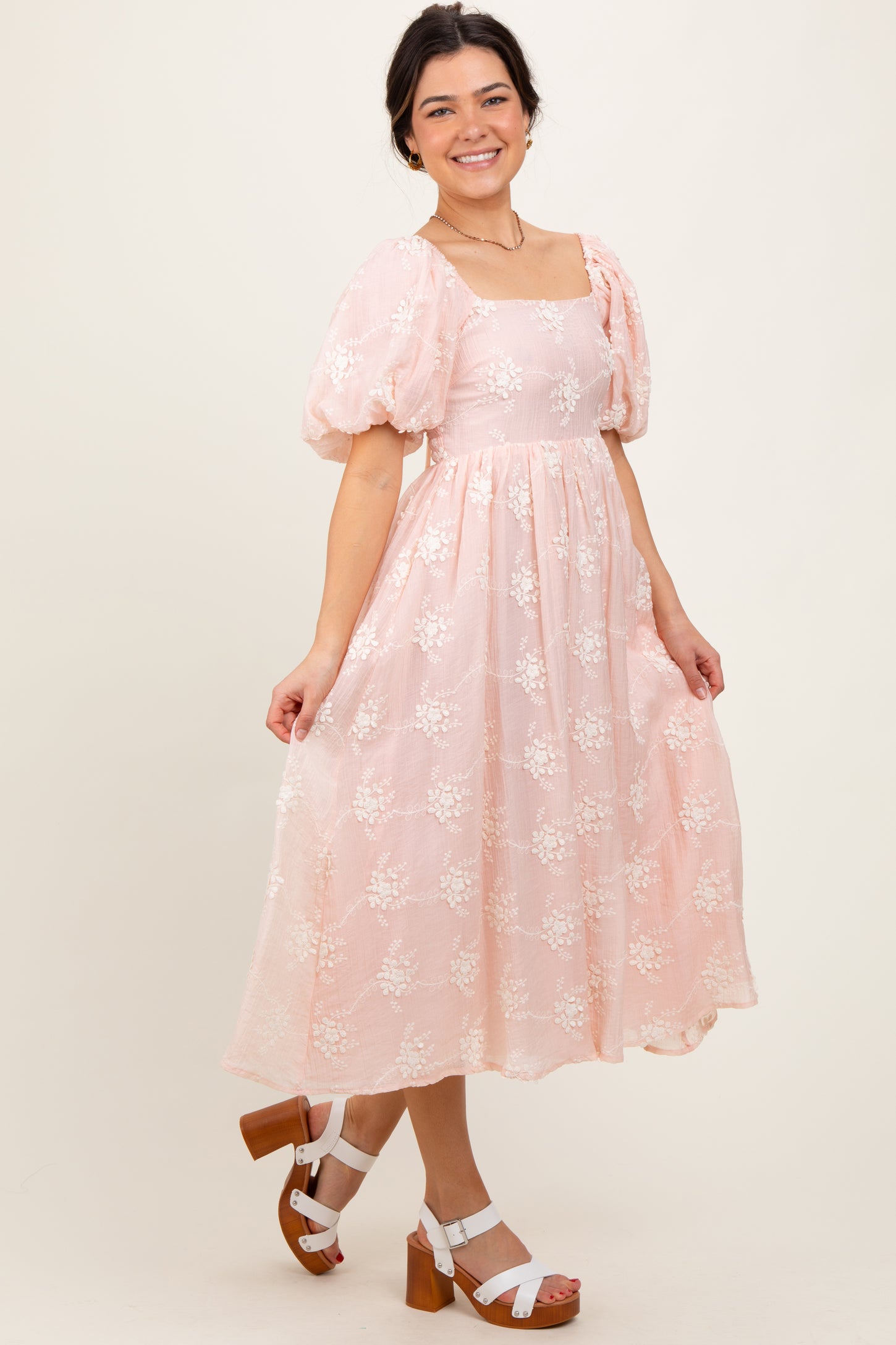 woman wearing a pink floral midi dress with puff sleeves and a square neckline, posing with a smile