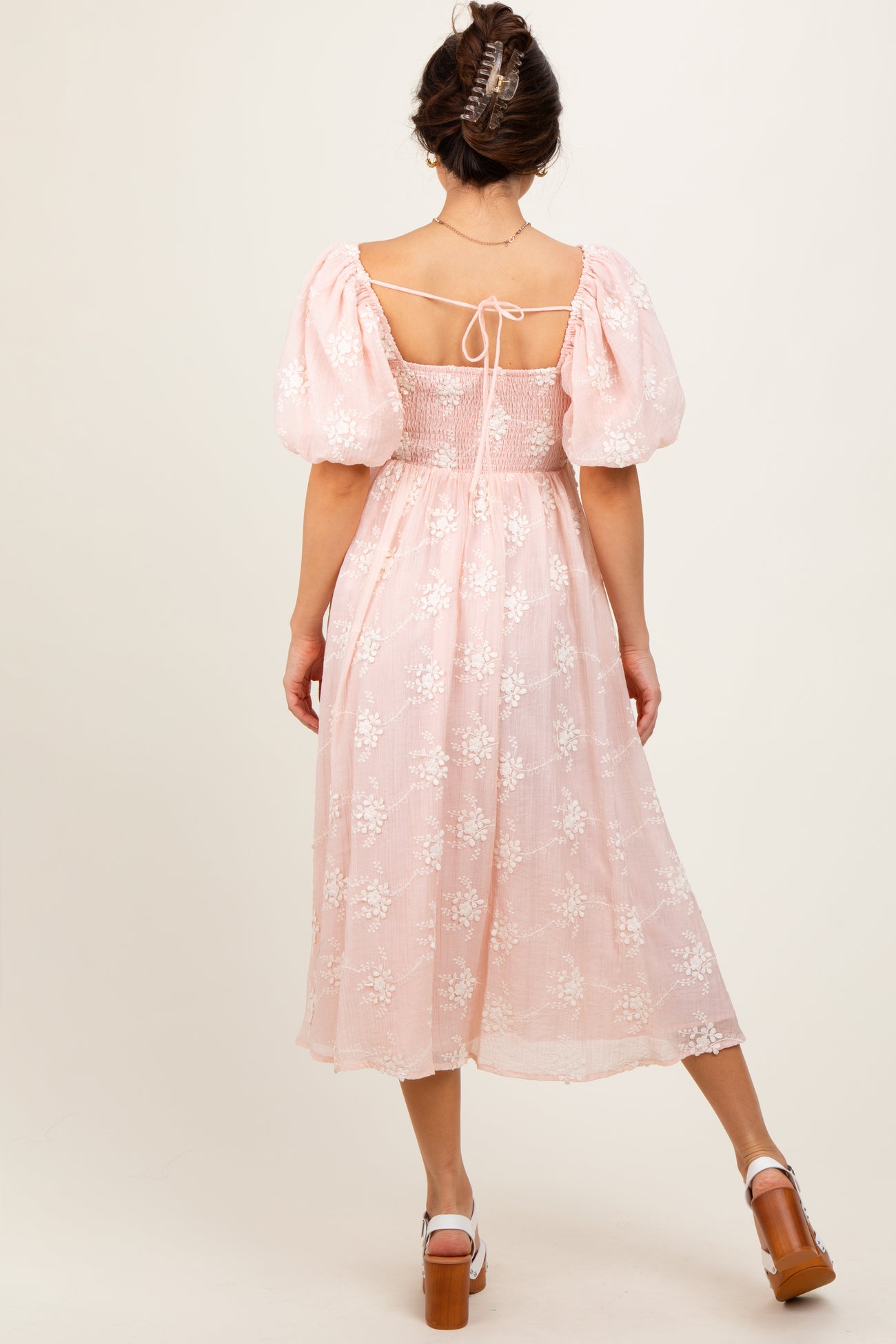 woman wearing a pink puff sleeve midi dress with floral embroidery and an open back detail