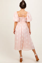 woman wearing a pink puff sleeve midi dress with floral embroidery and an open back detail
