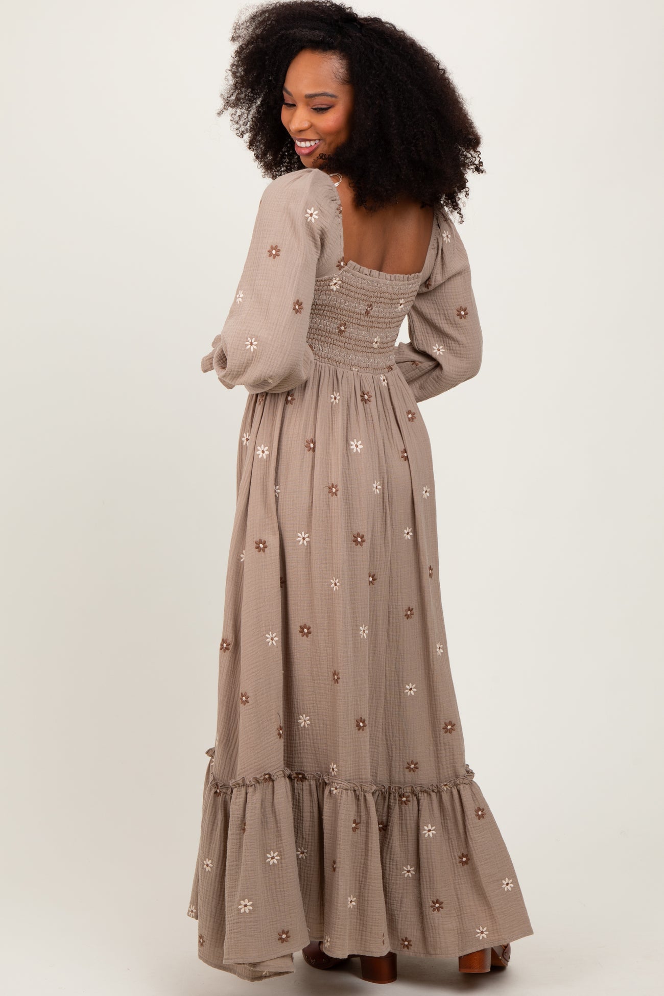 woman wearing a long brown floral embroidered maxi dress with puff sleeves and a tiered hem, showing the back view