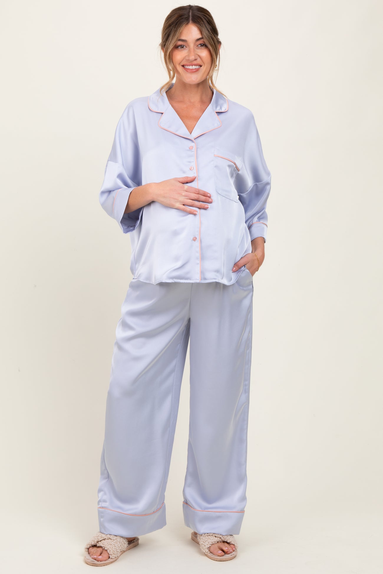 woman wearing a light purple satin maternity pajama set with a baby bump visible, featuring a pocket and pink piping details