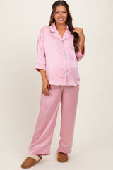 woman wearing a light pink satin maternity pajama set with a button-up top and loose-fitting pants, showing her baby bump