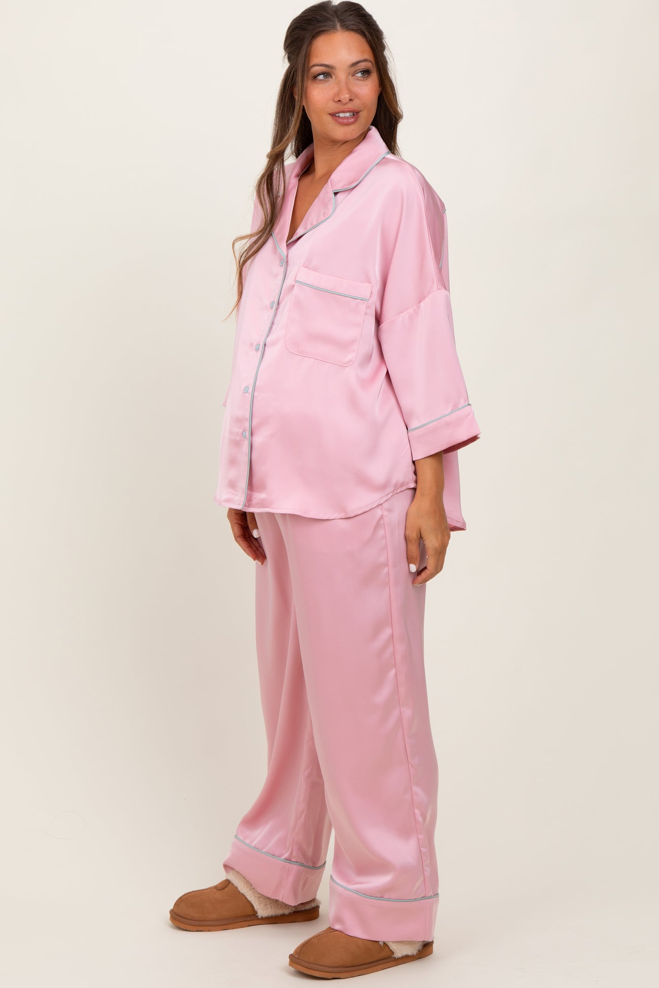 woman wearing a pink satin maternity pajama set with a button-up top and loose-fitting pants, showing her baby bump