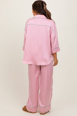 woman wearing a pink satin maternity pajama set with a relaxed fit and contrast piping, viewed from the back