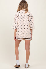 woman wearing a cream maternity pajama set with a geometric print, featuring a button-up top and shorts