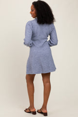 woman wearing a light blue long sleeve dress with a relaxed fit and back details, standing with her back to the camera