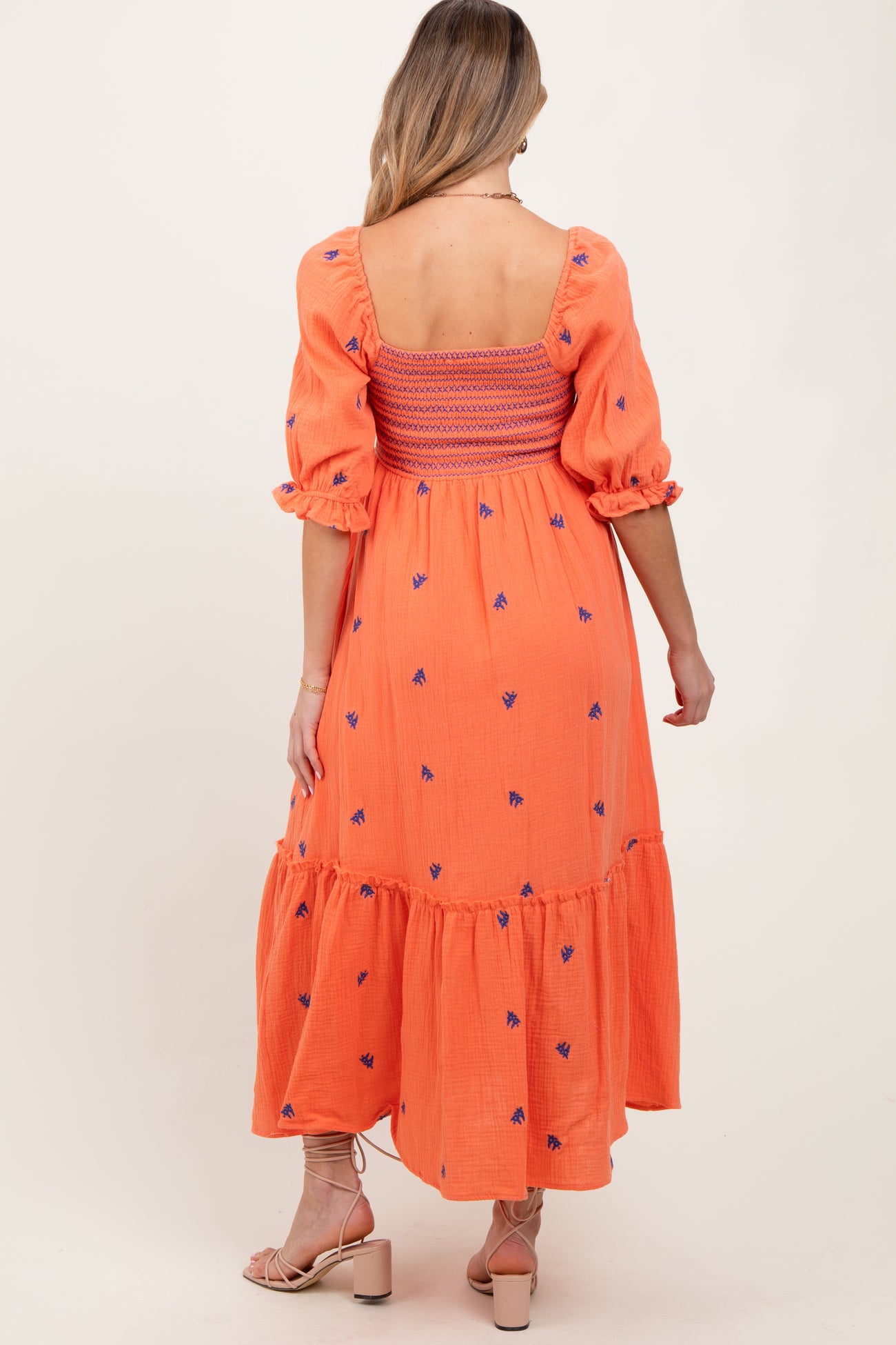 woman wearing an orange maternity dress with puff sleeves and floral embroidery, displayed from the back