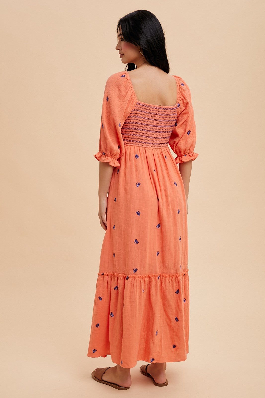 woman wearing an orange maxi dress with puff sleeves and floral embroidery, showing a smocked back and tiered hemline