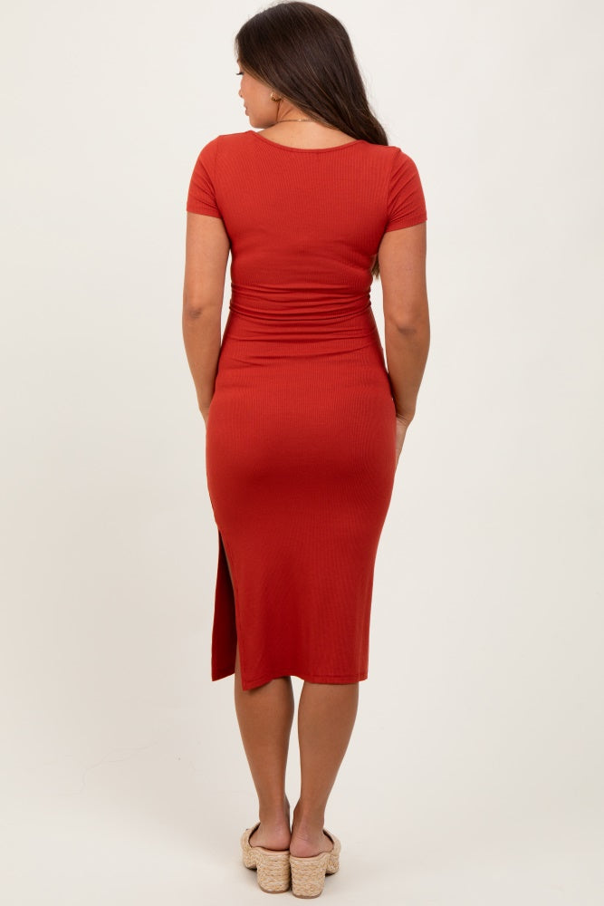 woman wearing a rust-colored maternity dress with a fitted silhouette and a side slit, showing her baby bump