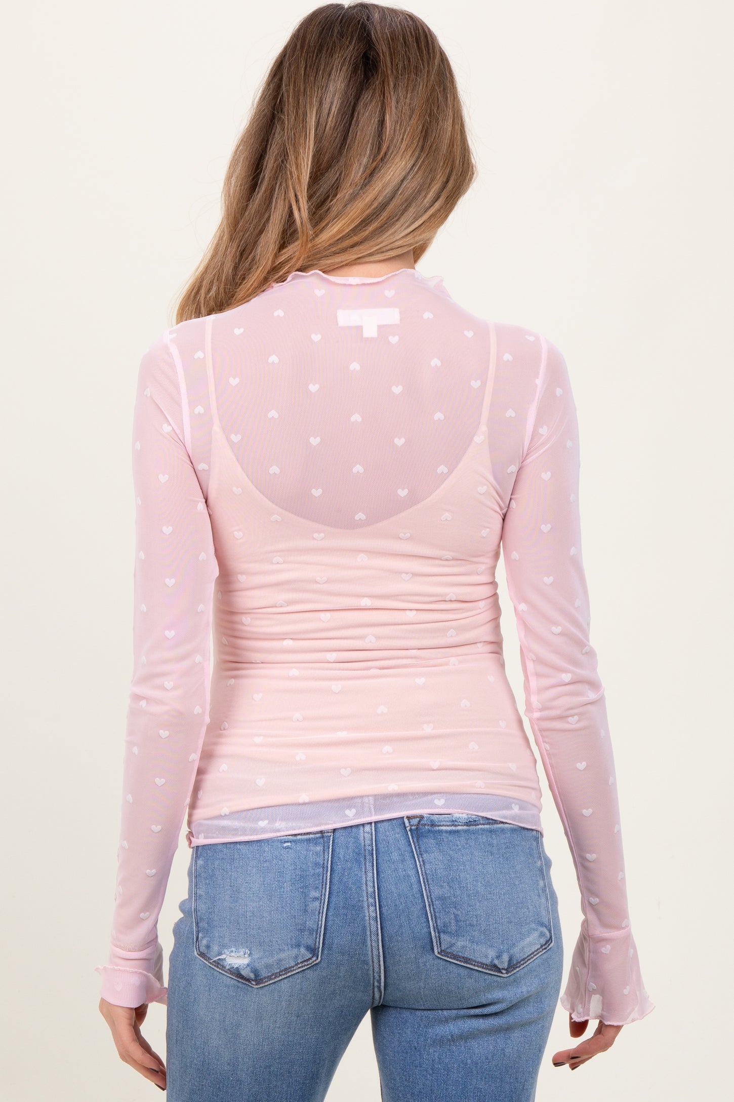 woman wearing a light pink long sleeve maternity top with heart patterns, showing a baby bump from the back