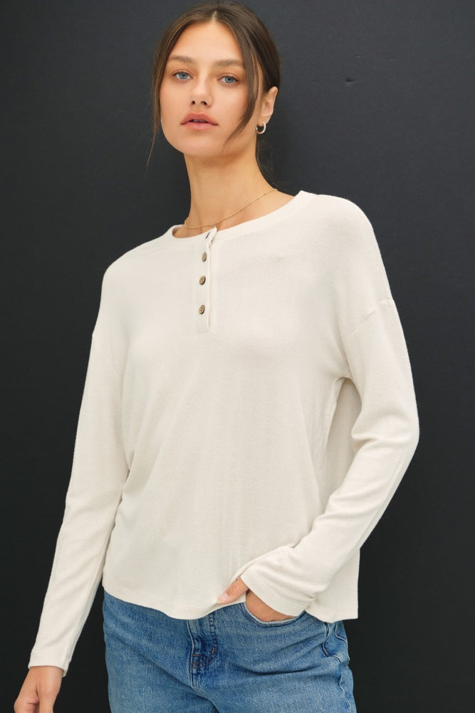 woman wearing a cream long sleeve henley top with three buttons and a relaxed fit paired with blue jeans