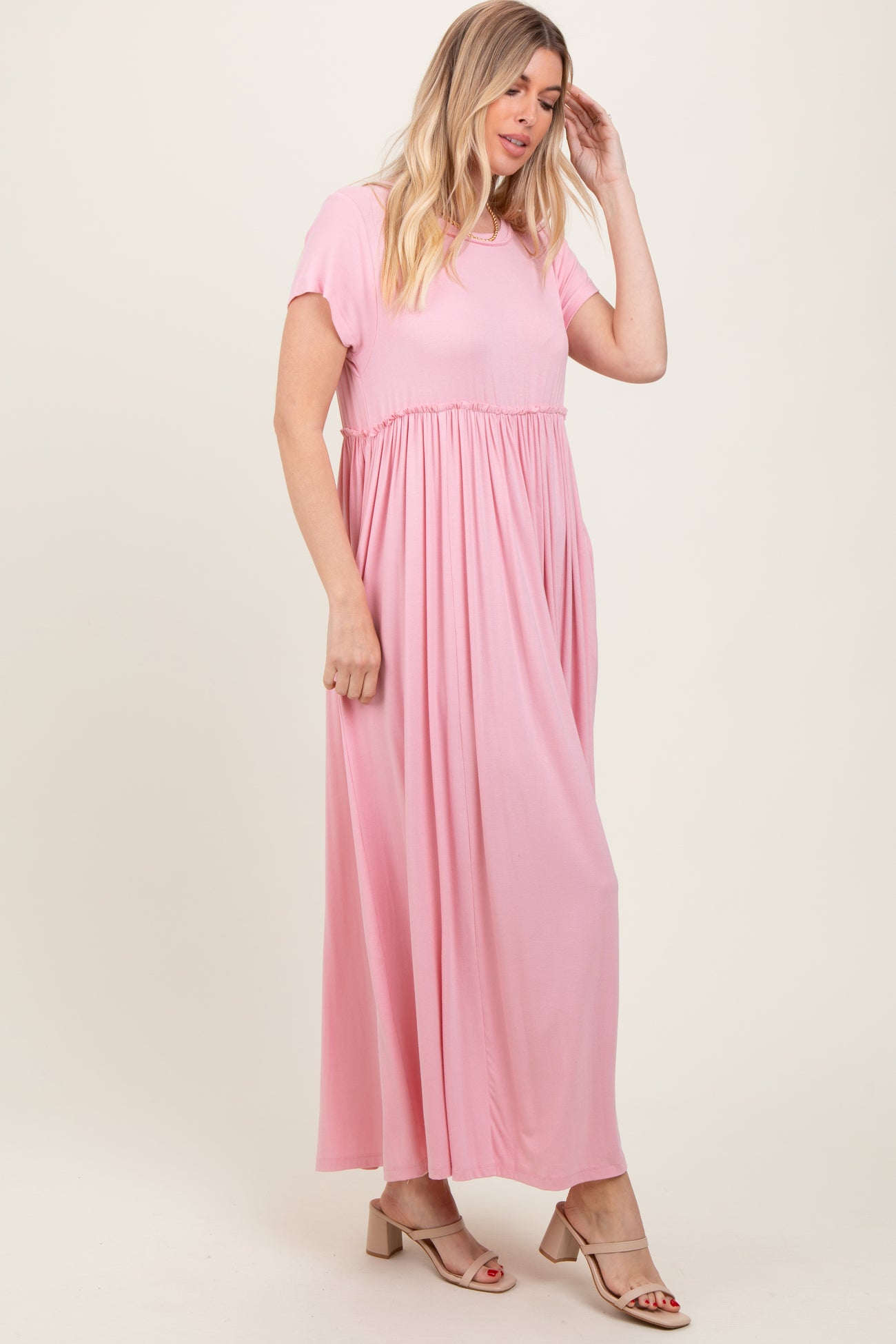 woman wearing a light pink maxi dress with short sleeves and a gathered waist, standing sideways