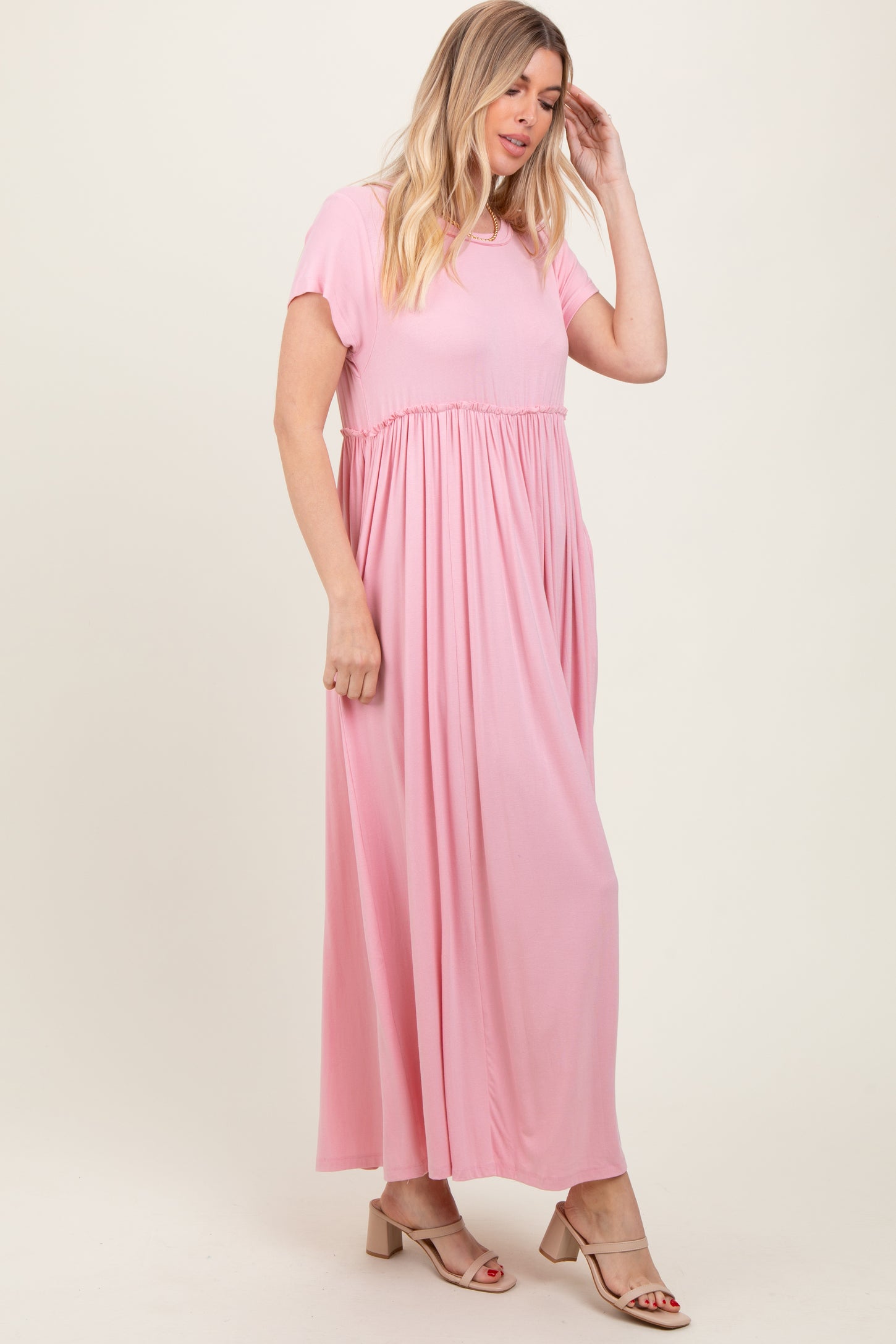 woman wearing a light pink maxi dress with short sleeves and a gathered waist, standing sideways