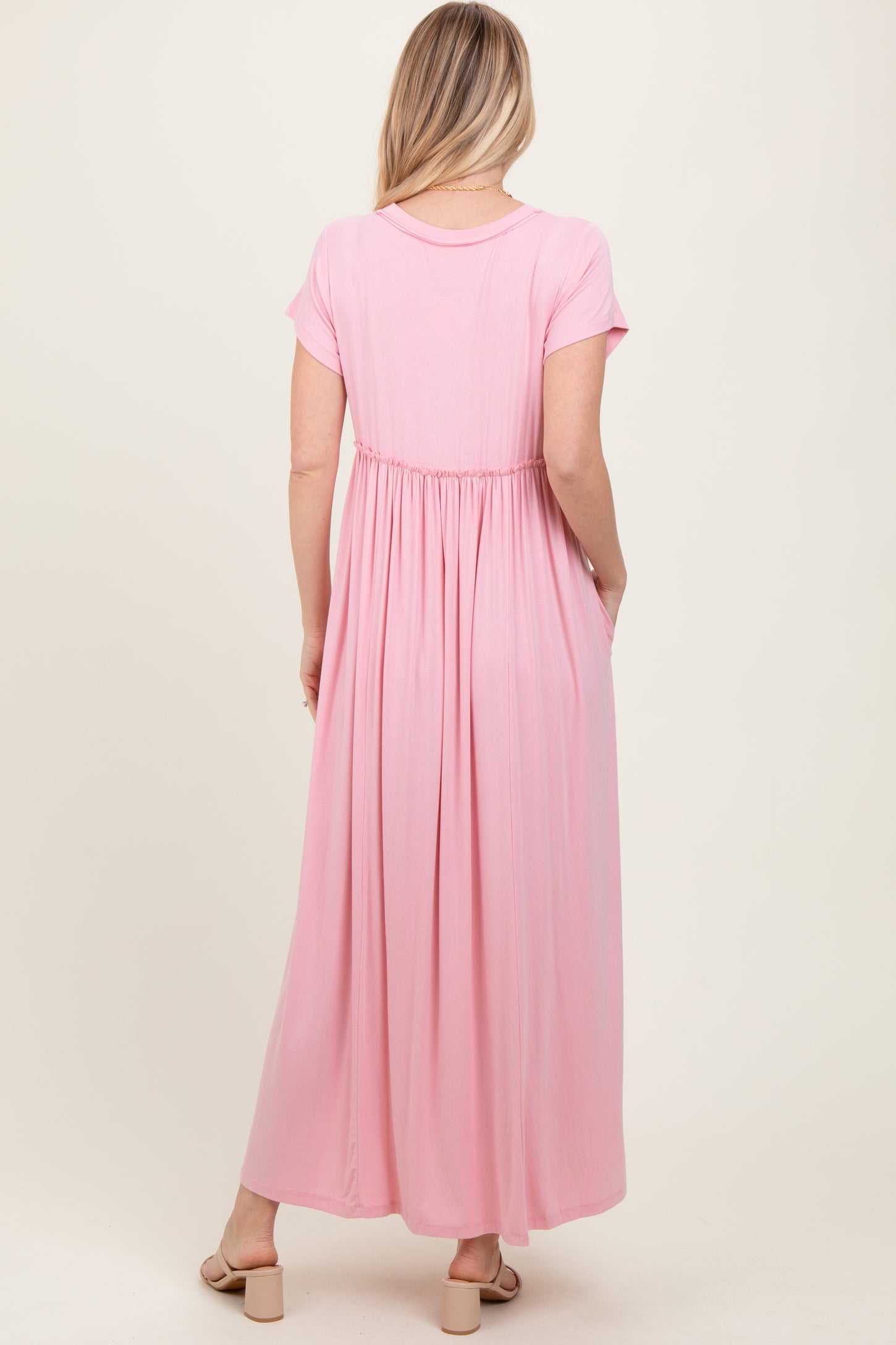 woman wearing a light pink short sleeve maxi dress with an elastic waistband and side pockets, viewed from the back