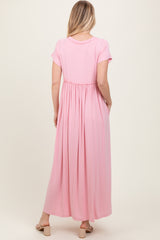 woman wearing a light pink short sleeve maxi dress with an elastic waistband and side pockets, viewed from the back