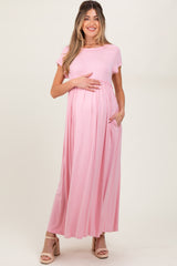 woman wearing a light pink short sleeve maternity maxi dress and holding her baby bump