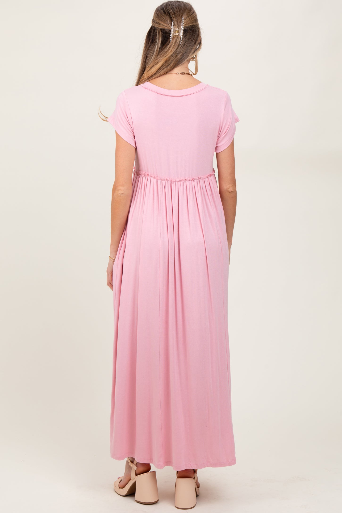 woman wearing a pink maternity maxi dress with short sleeves and an empire waist, showing a baby bump