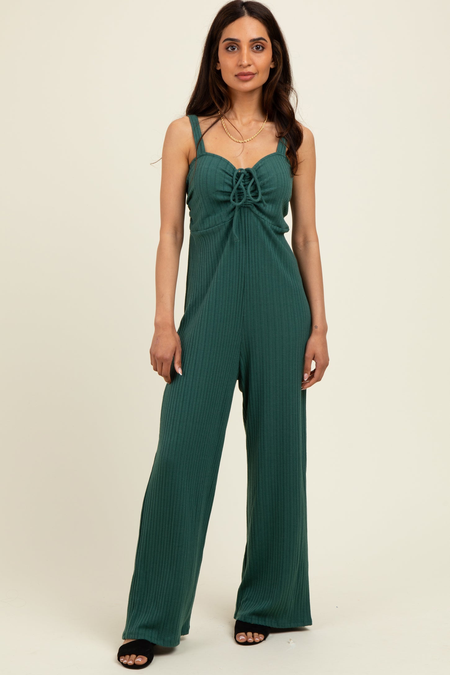 woman wearing a green ribbed jumpsuit with a front tie detail and spaghetti straps